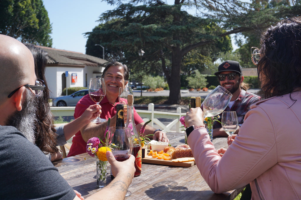 Group of people at an outdoor table drinking wine and eating a cheese plate - example of a private wine event