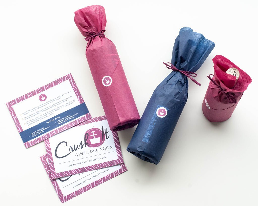 three wine bottles gift wrapped in Crush It brand colors with Crush It Wine Education postcards and promotional materials