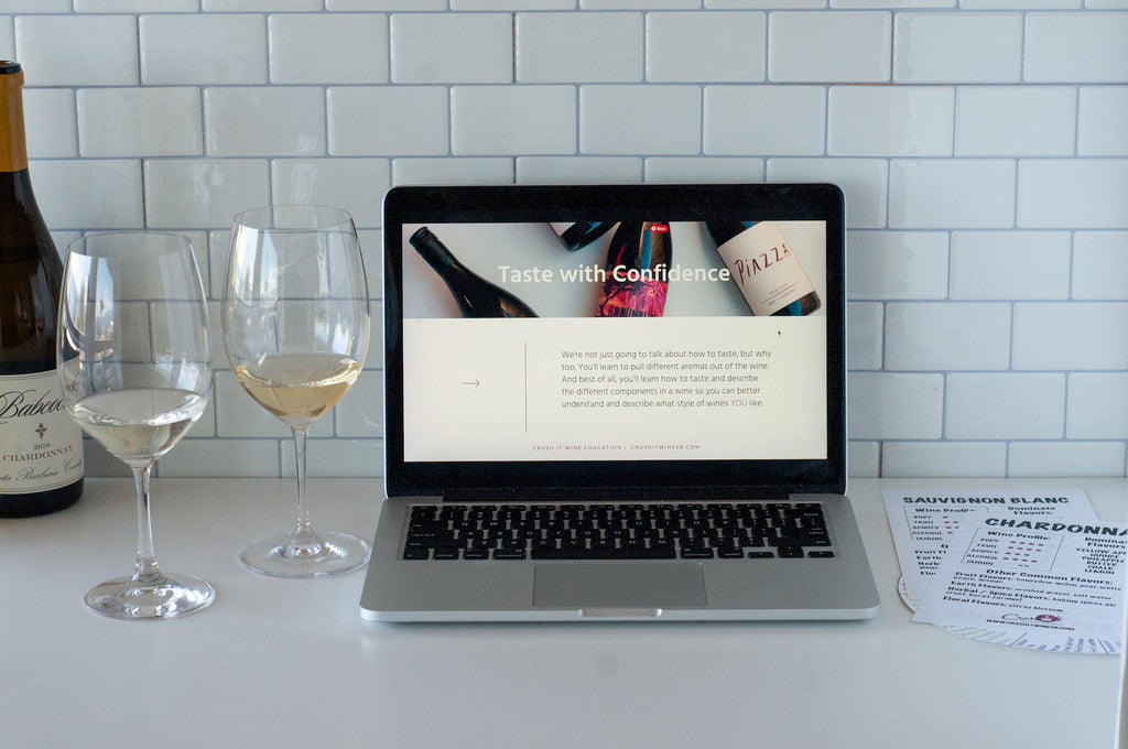 Bottle of Chardonnay in the background with two different glasses of white wine next to a laptop computer displaying a slide from Wine is For Everyone - A wine tasting for beginners course and custom wine class materials